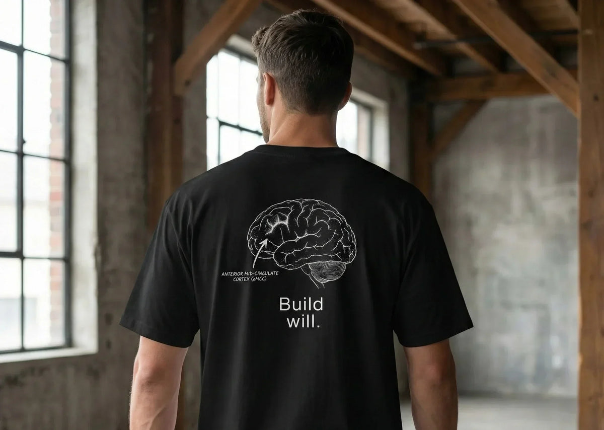 a man seen form behind wears a black t shirt with white Build Will graphic highlighting the anterior mid cingulate cortex, an area of the brain that grows when you do hard things