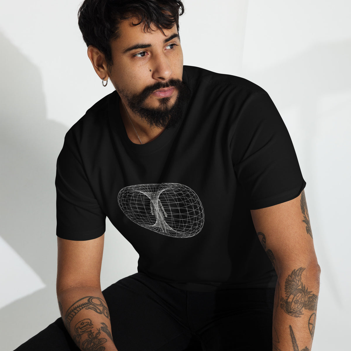 Man with goatee and tattoos wearing a black heavyweight all cotton t-shirt printed with the human toroidal field