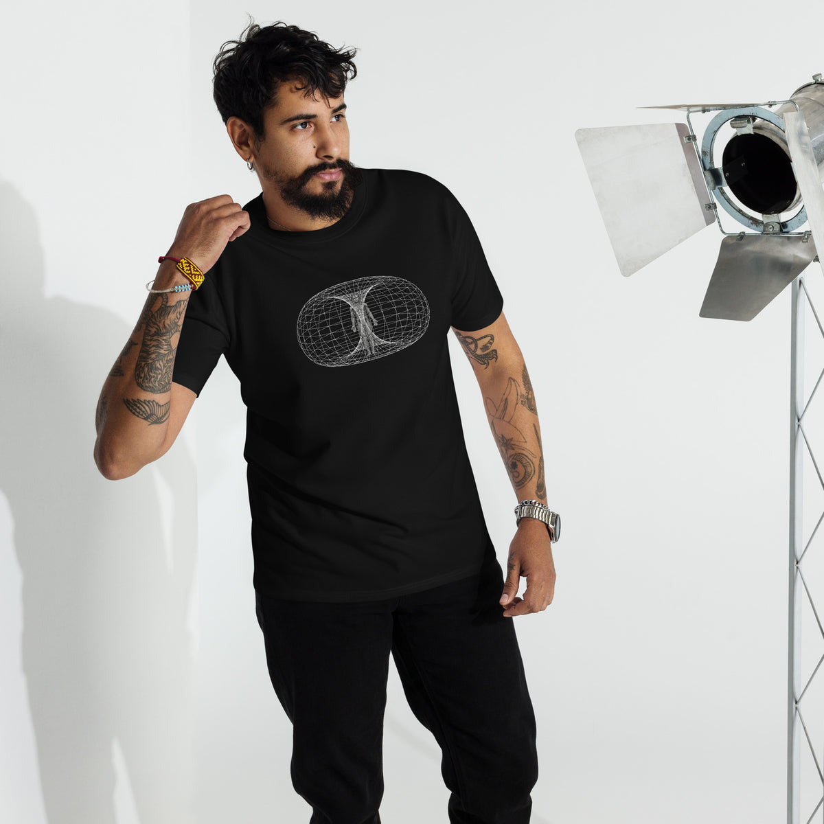 Man standing in a black heavyweight all t-shirt printed with the human toroidal field in a studio setting against a white background