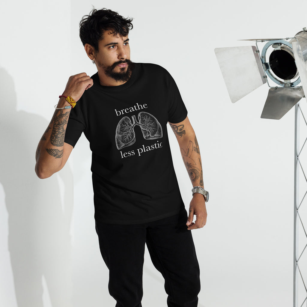 Man with tattoos wearing a black black 100 percent cotton heavyweight t-shirt printed with a vintage style line drawing of human lungs and the words Breathe Less Plastic in a studio setting on a whitebackgroundf
