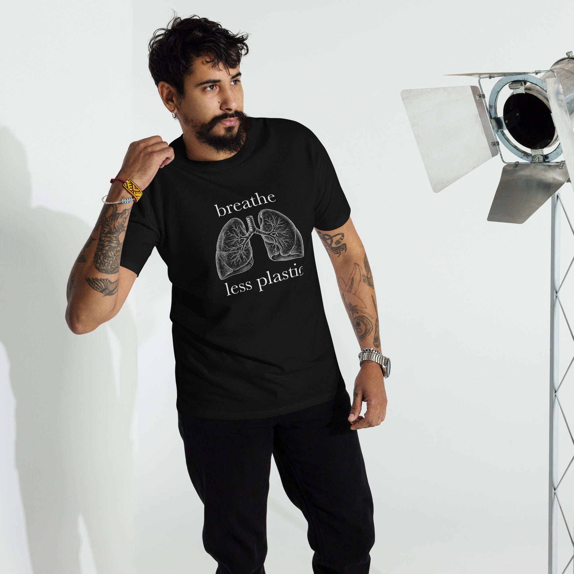 Man with tattoos wearing a black black 100 percent cotton heavyweight t-shirt printed with a vintage style line drawing of human lungs and the words Breathe Less Plastic in a studio setting on a whitebackgroundf