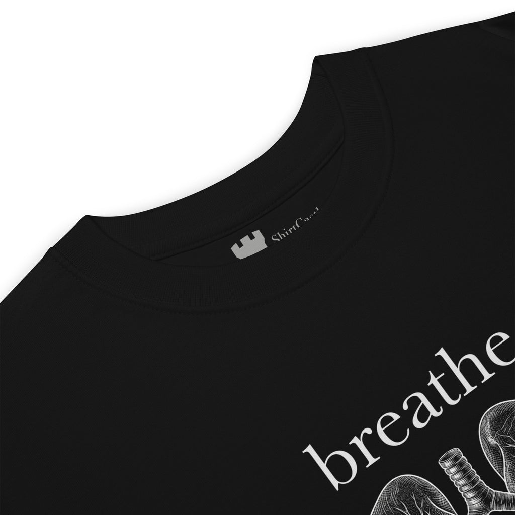 Close-up of a black crewneck t-shirt showing the inner neck ShirtCastle label and part of a white graphic print on the front with the word breathe and anatomical lungs.