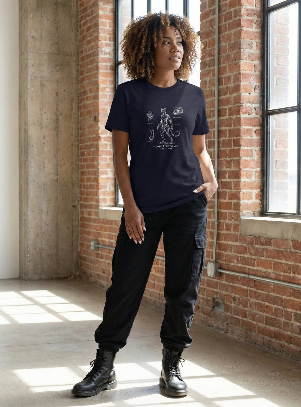 Person wearing a black t-shirt with a design, standing in a room with brick walls and large windows.