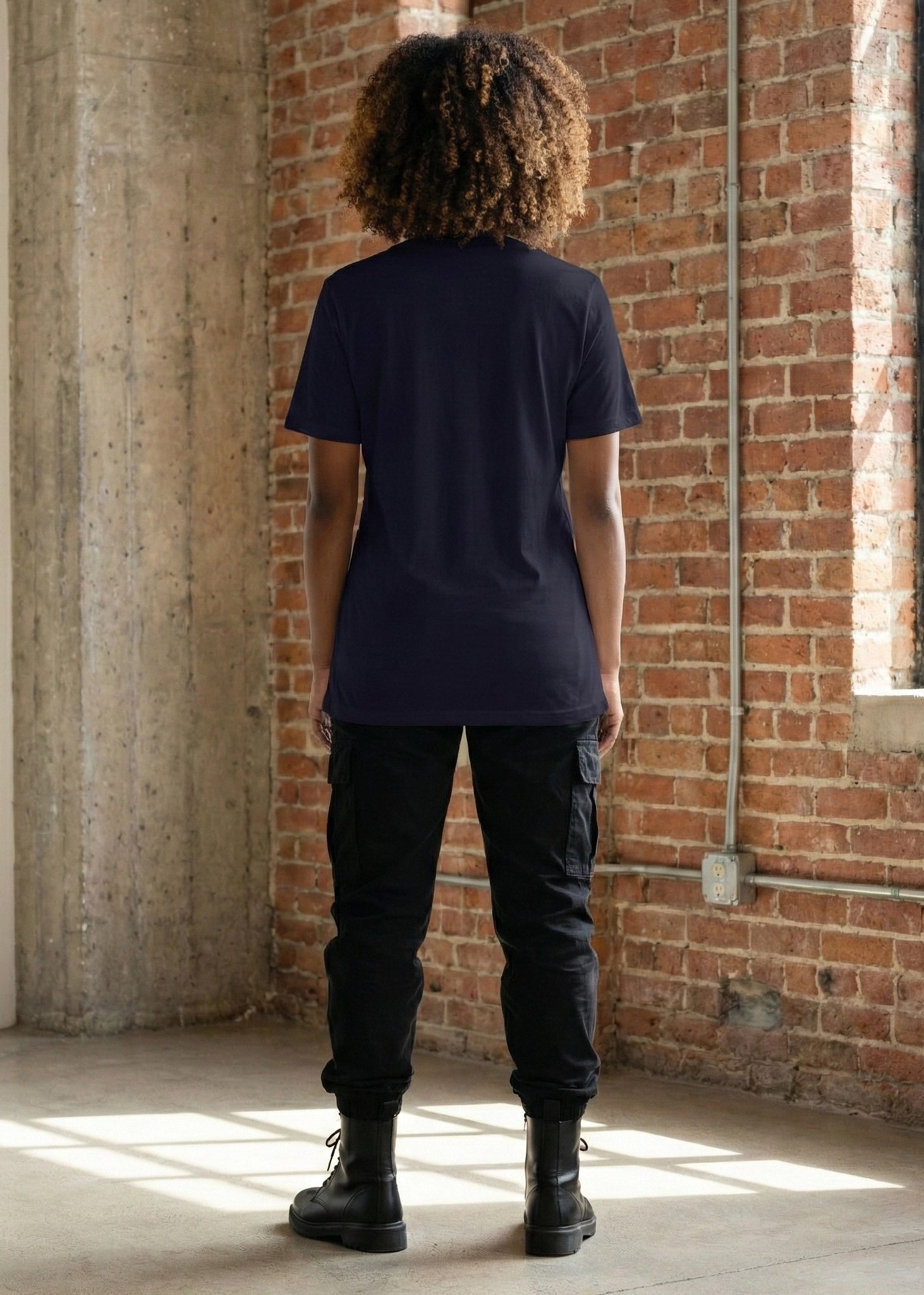 a model wears a blue womens relaxed fit t shirt shown from behind with a brick background