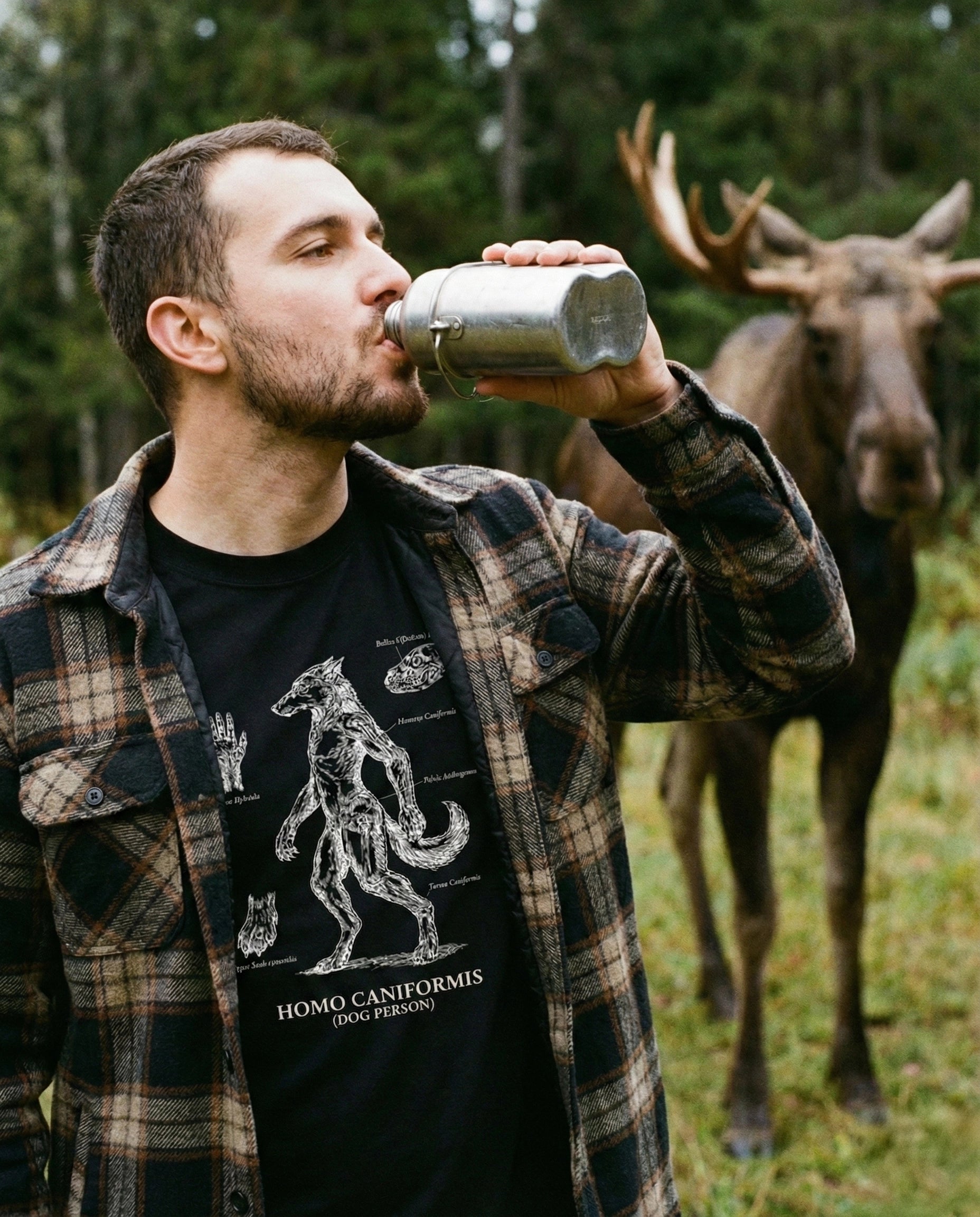 Man drinking from a metal cup with a moose in the background