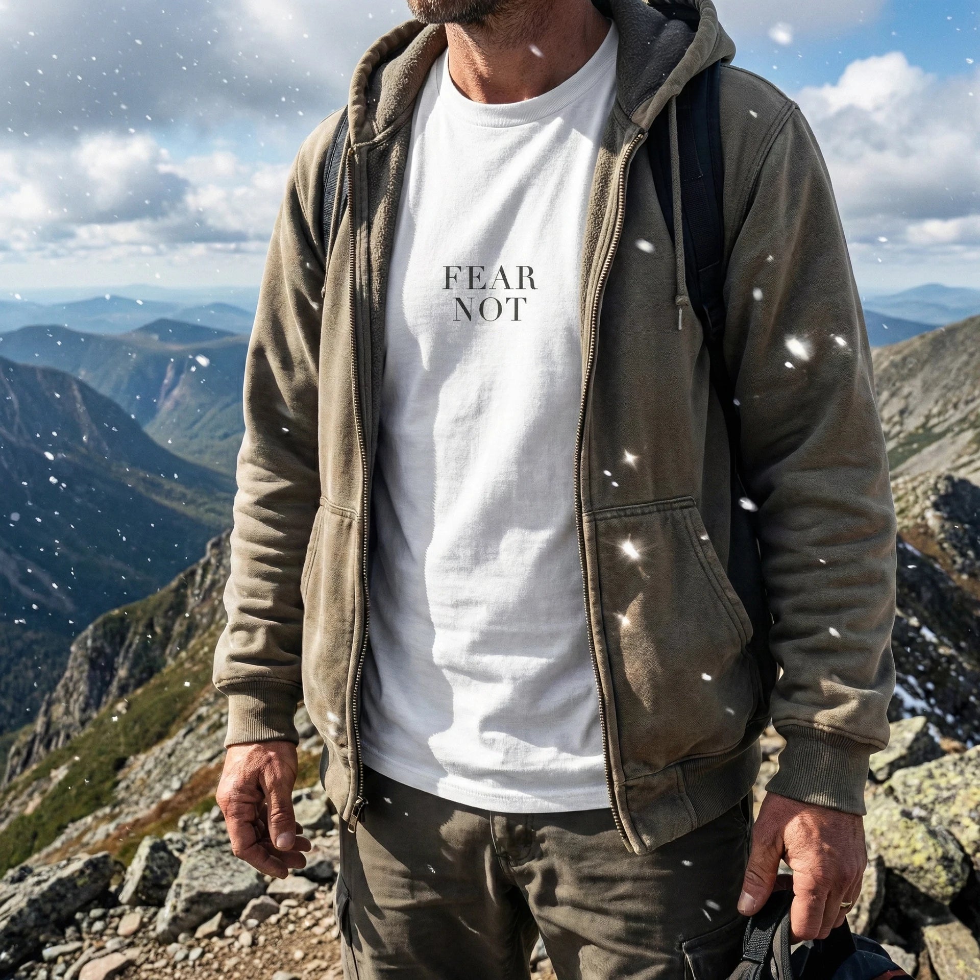 Person standing on a mountain with 'FEAR NOT' t-shirt, wearing a green jacket.