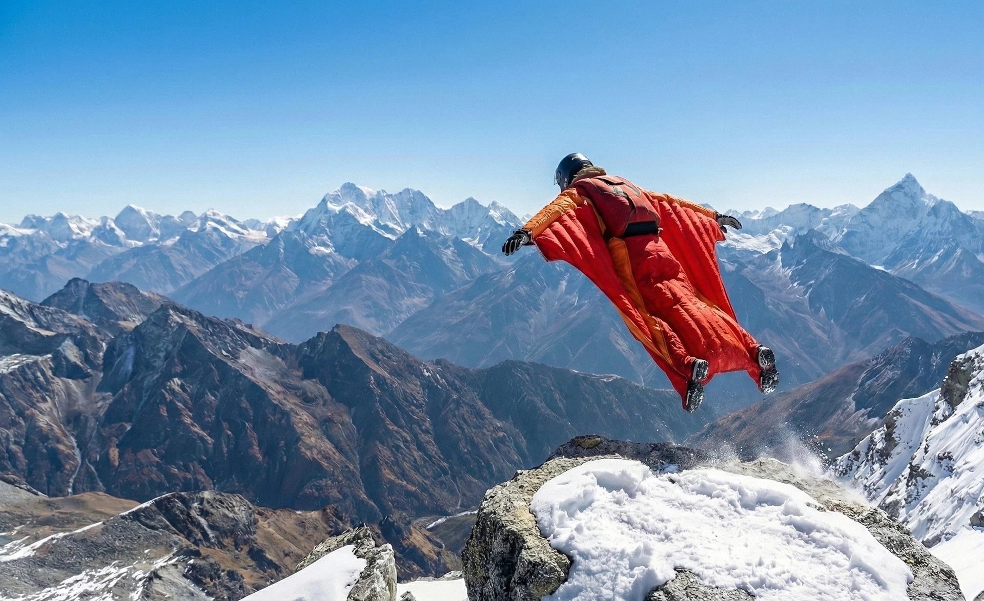 Person in a red cape flying over mountainous landscape with snow-capped peaks.
