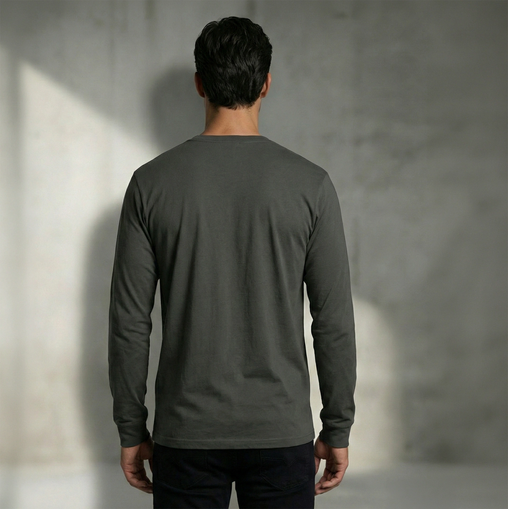 Man wearing a dark gray 185gsm ring-spun organic cotton long-sleeve shirt against a textured wall.