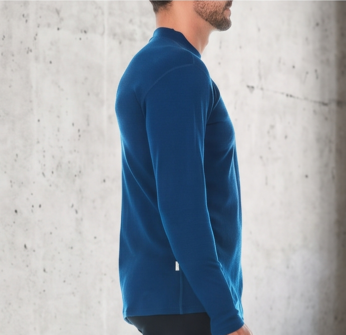 A man wearing a blue 100 percent merino wool mock neck shown from the side against a textured grey background.