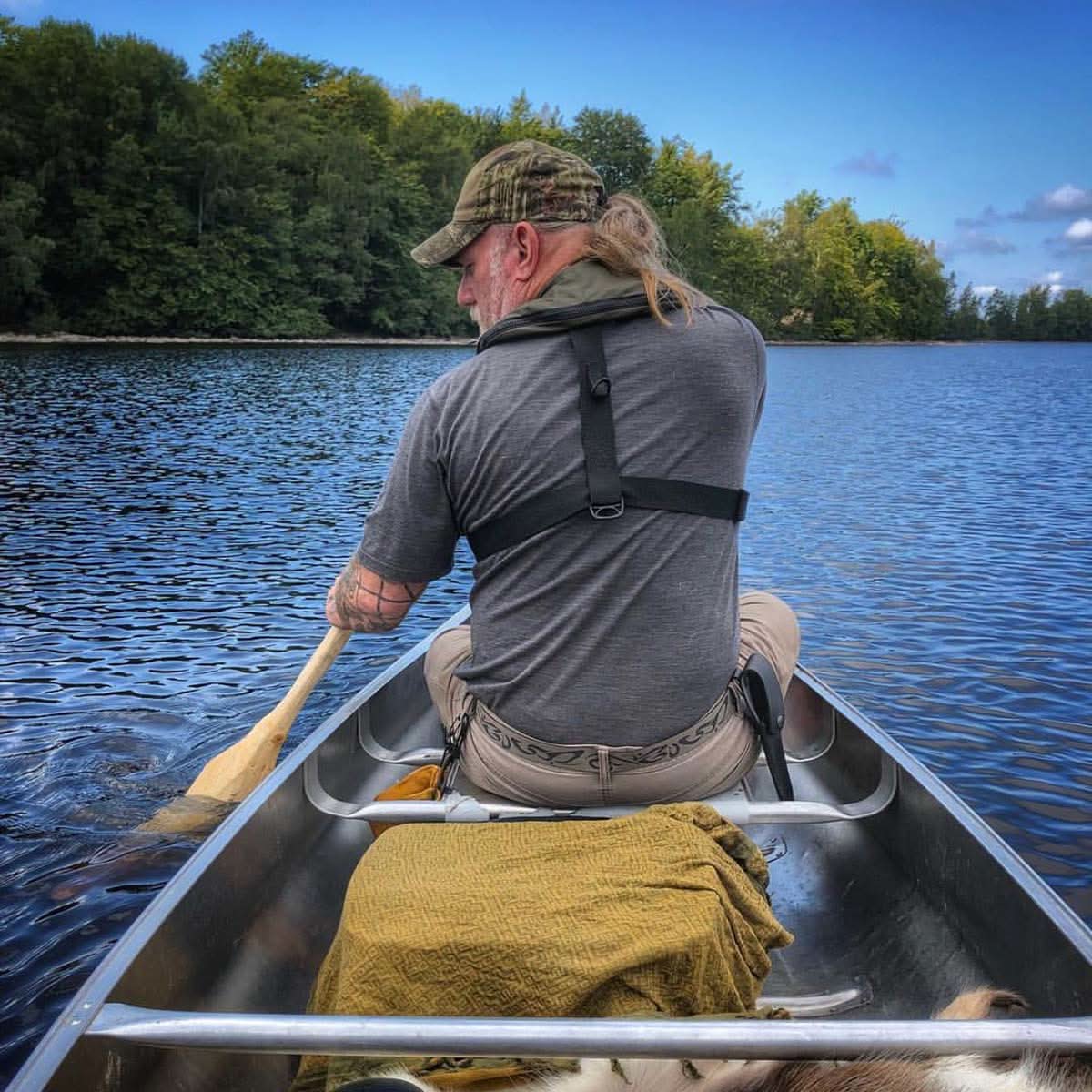 A man wearing a charcoal gray 100 percent merino wool t shirt paddling a canoe on a lake from behind.