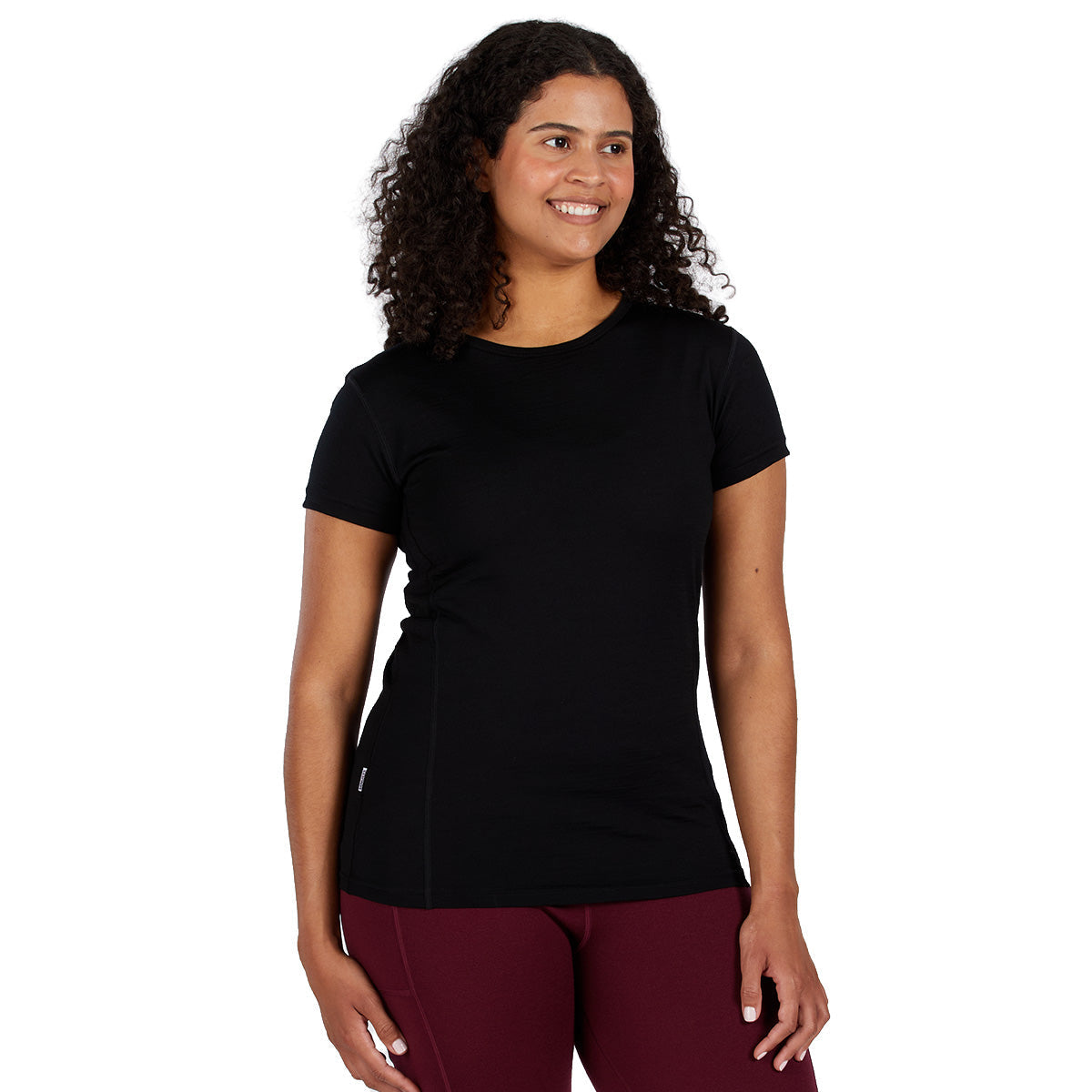 A smiling woman wearing a black 100 percent merino wool t shirt shown from the waist up against a solid white background.