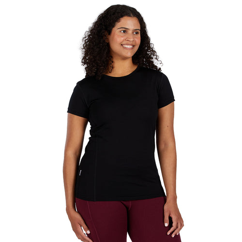 A smiling woman wearing a black 100 percent merino wool t shirt shown from the waist up against a solid white background.