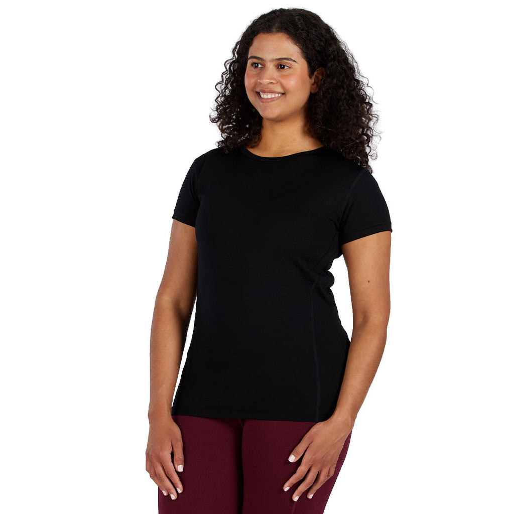 A woman wearing a black 100 percent merino wool t shirt shown from the waist up against a solid white background.