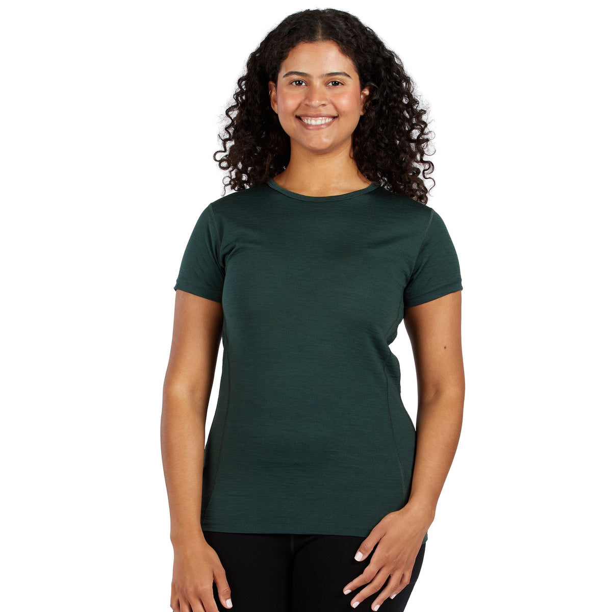 A smiling woman with dark curly shoulder length hair wearing a forest green 100 percent merino wool t shirt shown from the waist up against a solid white background.