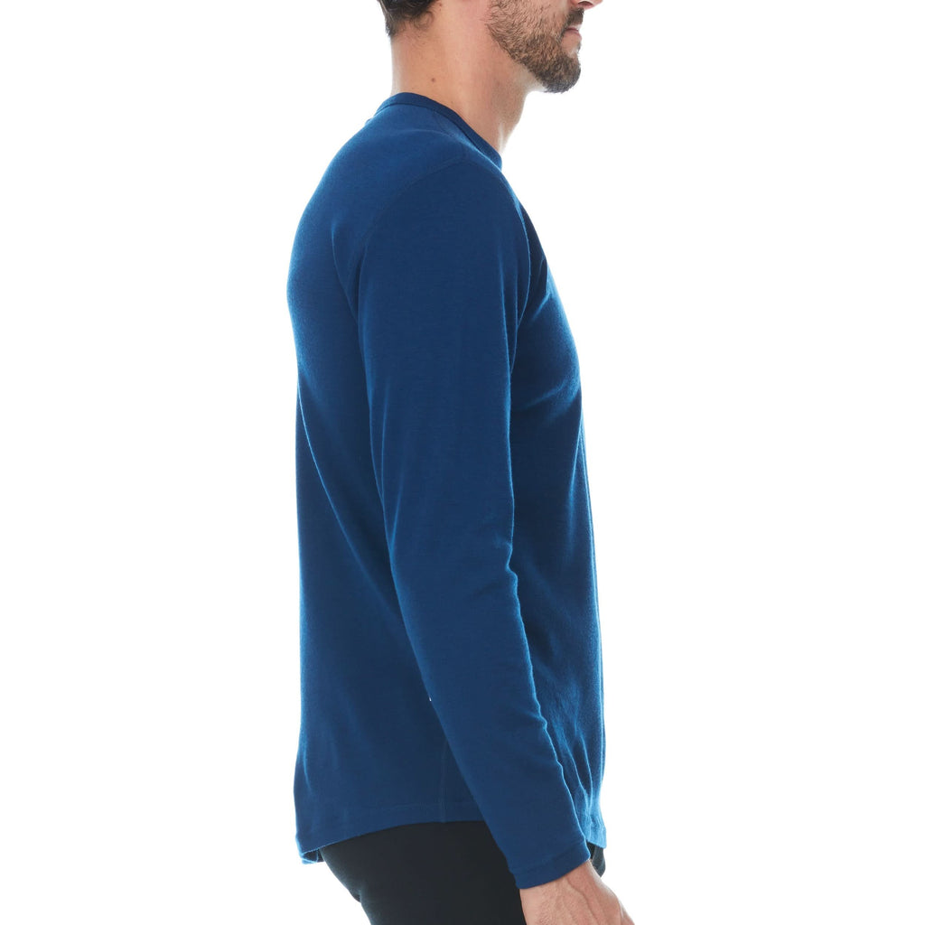 Man wearing a blue 100% merino wool base layer top against a white background - side view
