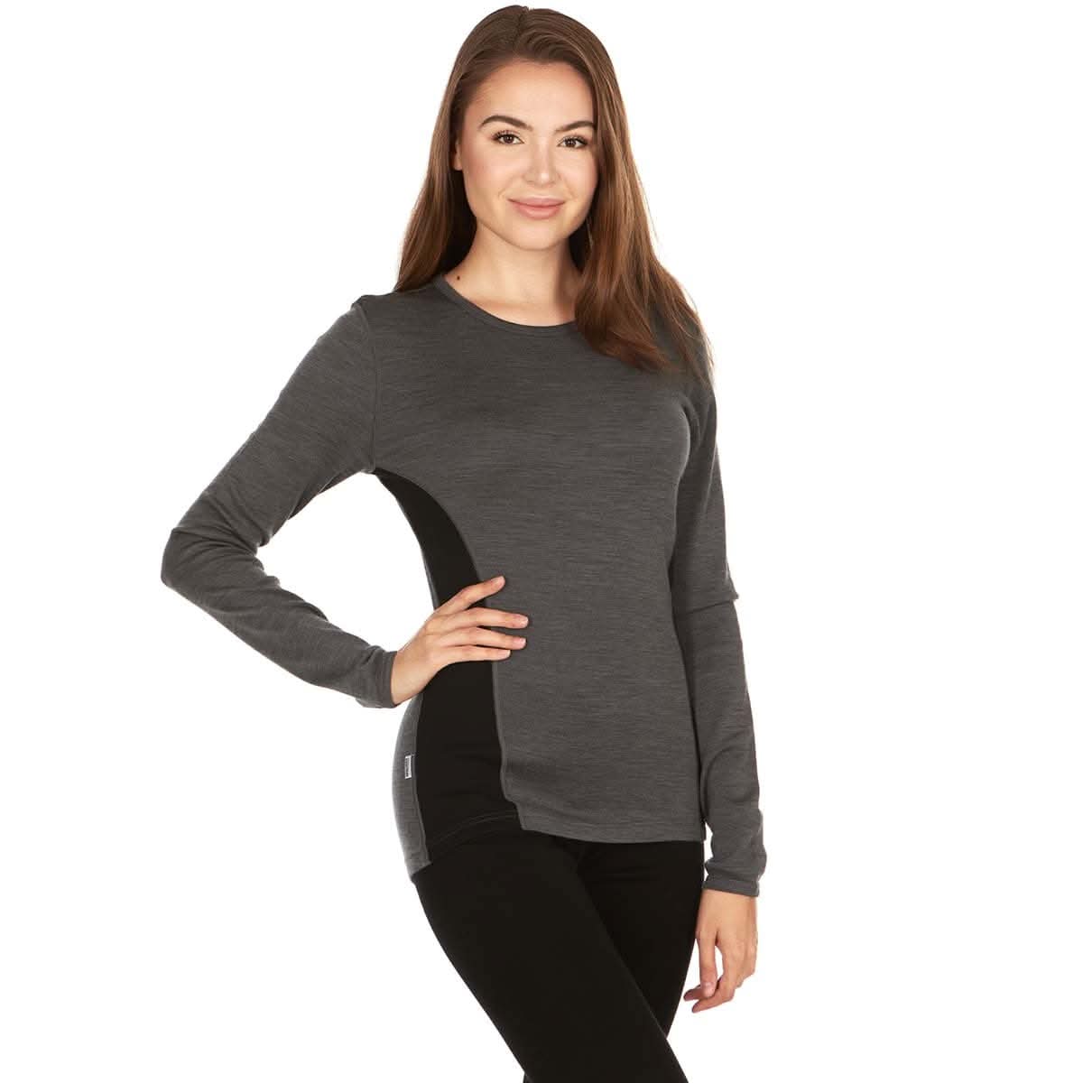 A woman modeling a two-tone dark gray long-sleeve 100 percent merino wool base layer top with black side panels, paired with black leggings, against a plain white background.