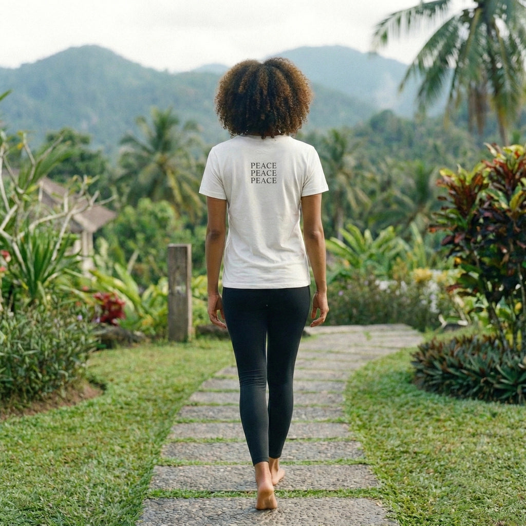 Person walking on a path in a lush green garden wearing a white t-shirt with 'PEACE PEACE' text.