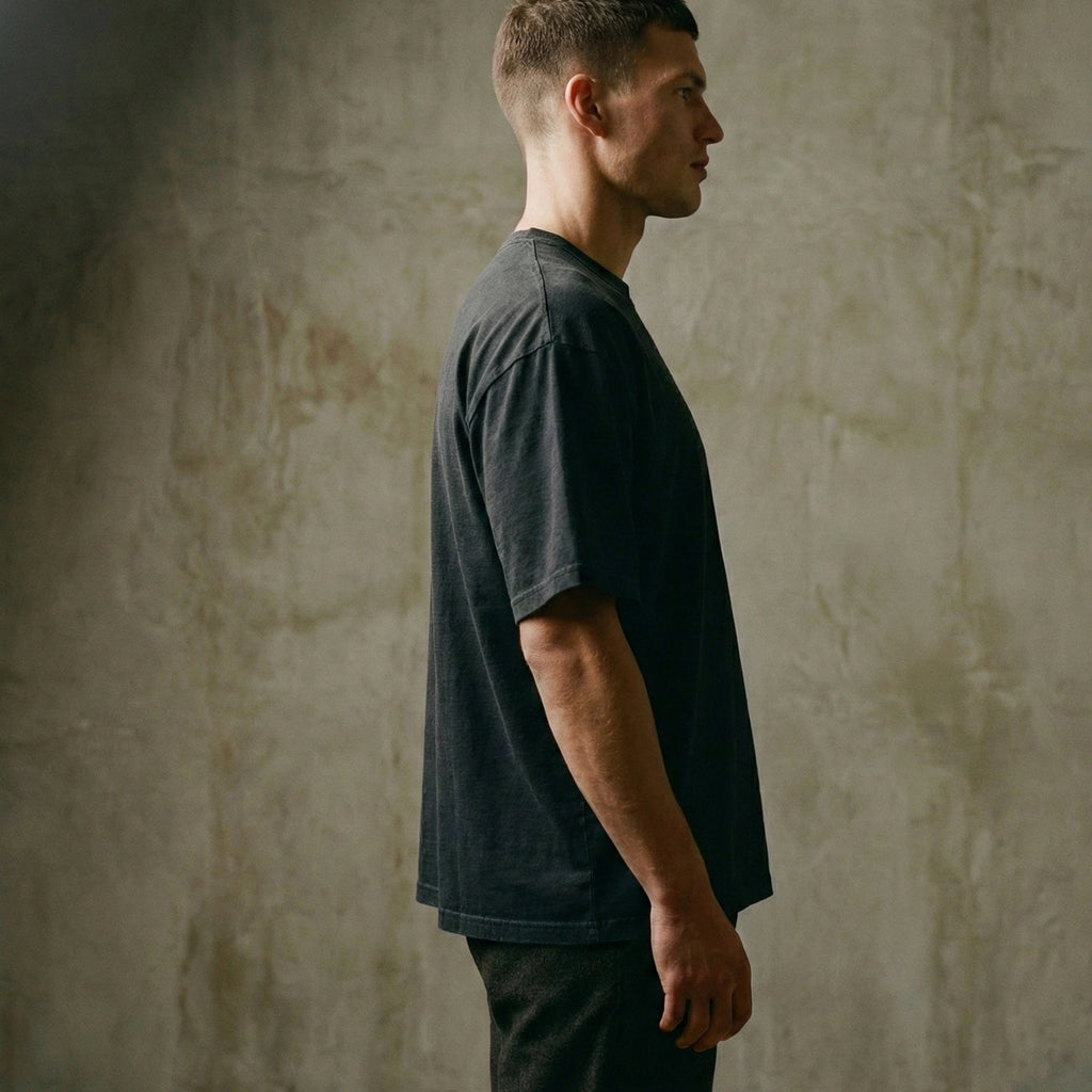 Man wearing a Man wearing a garment-dyed faded black oversized carded-cotton t-shirt against a concrete background - side view