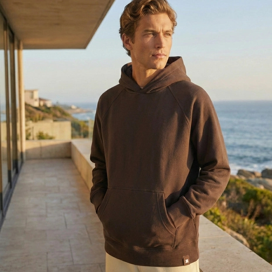 Man wearing a brown hoodie standing on a balcony with ocean view