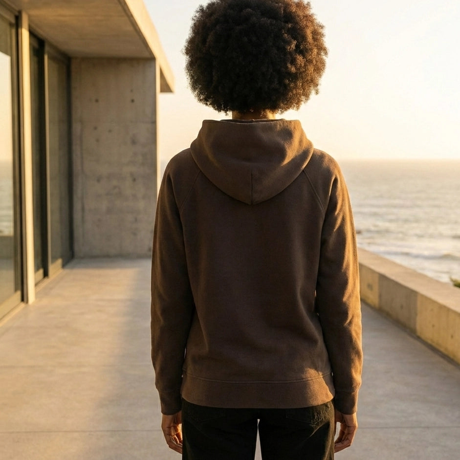 Person wearing a brown 500sgm organic cotton hoodie standing on a rooftop with a cityscape in the background