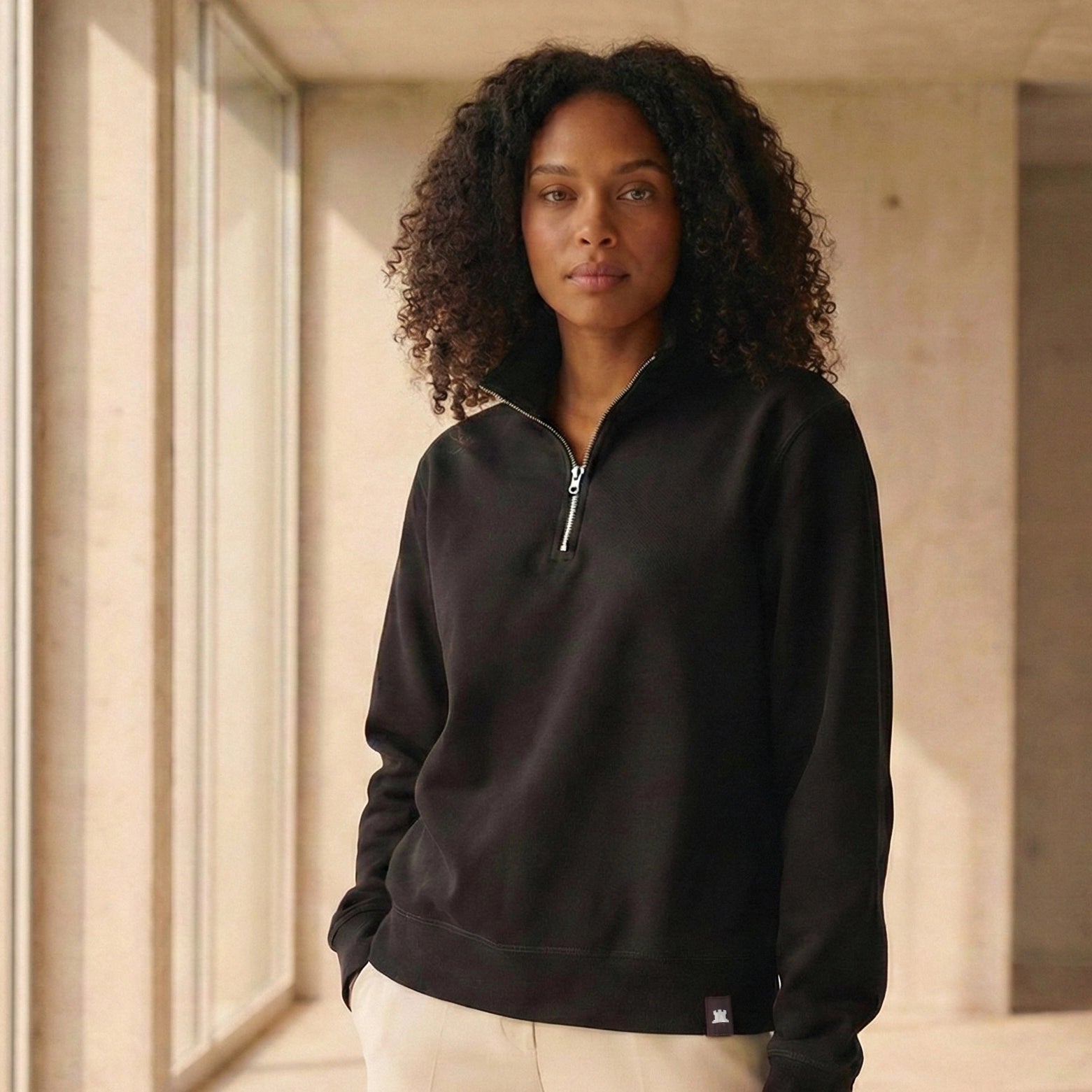 Woman wearing a black organic cotton quarter-zip sweatshirt standing indoors with a neutral background