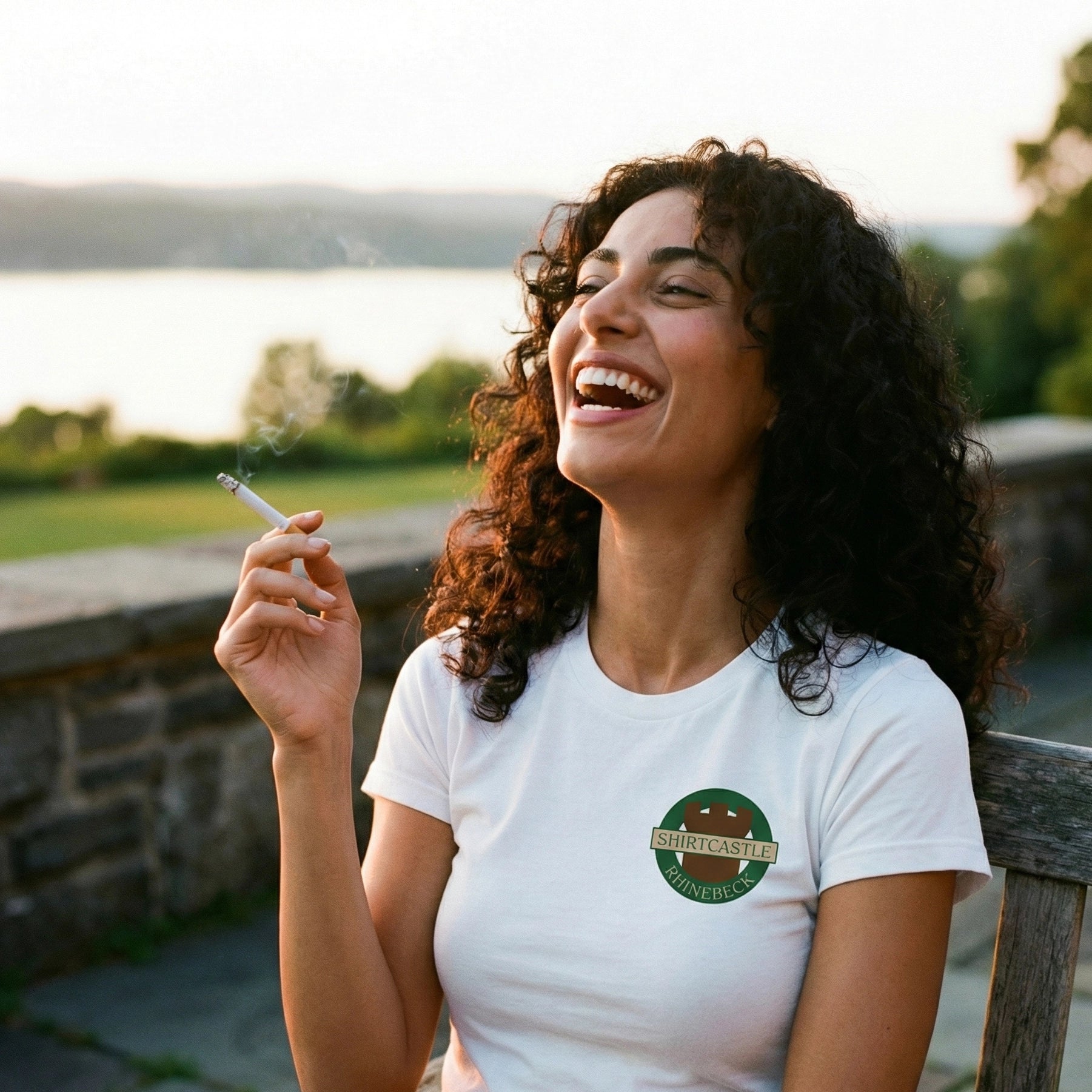 Woman laughing outdoors with a scenic background, wearing a white shirtcastle rhinebeck  t-shirt 