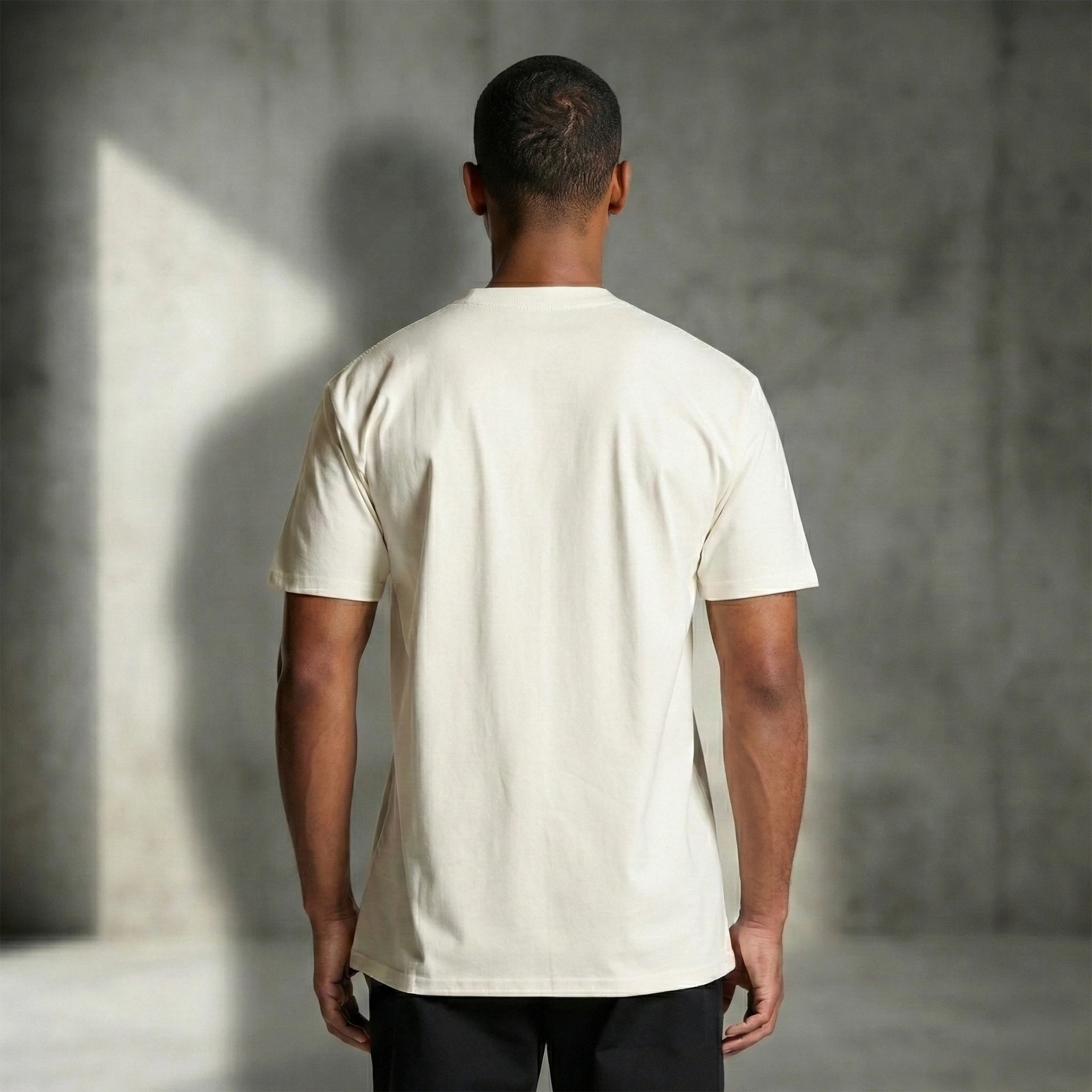 Man wearing a plain white t-shirt against a gray concrete wall.