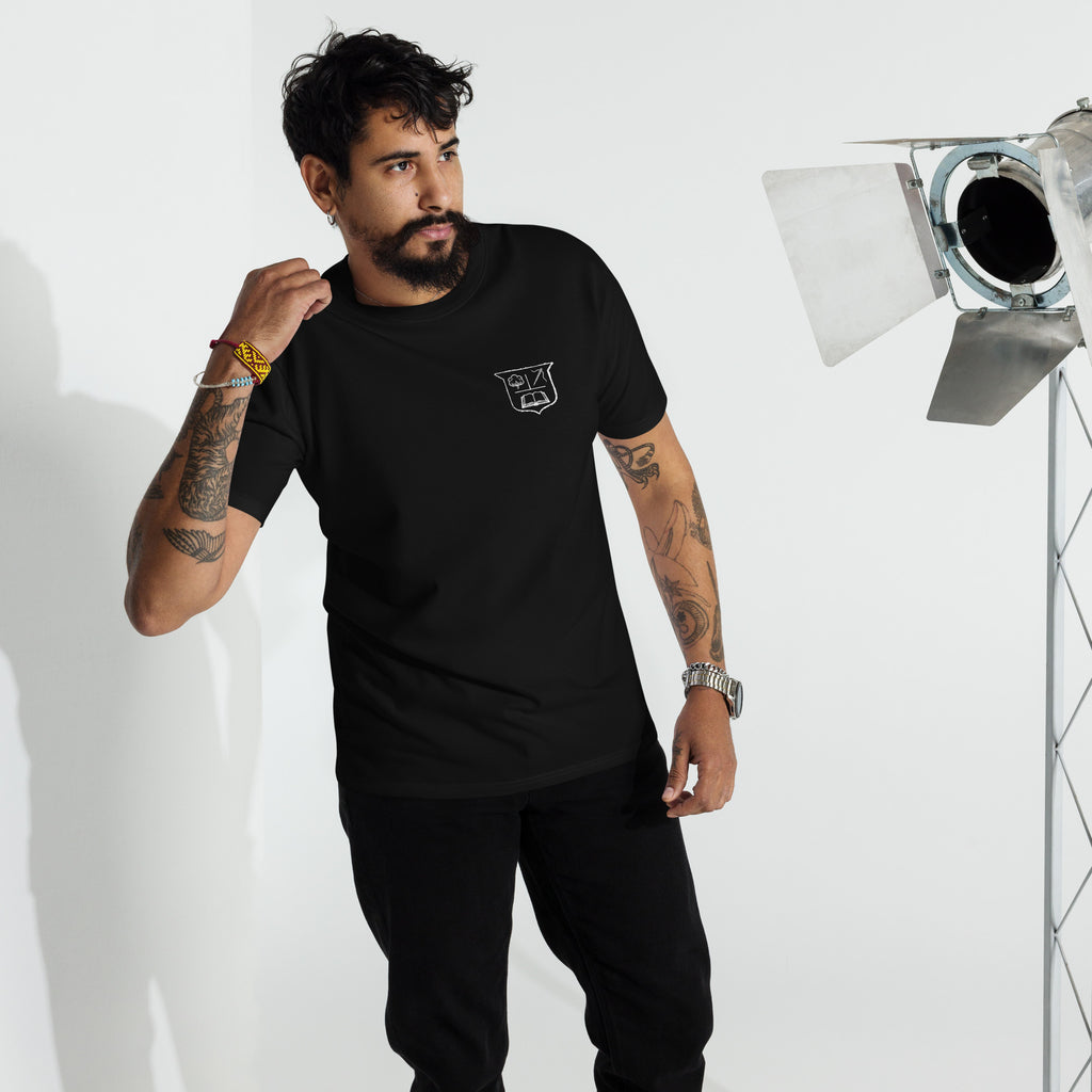 Man wearing a black t-shirt with a white crest on the left breast in a studio setting