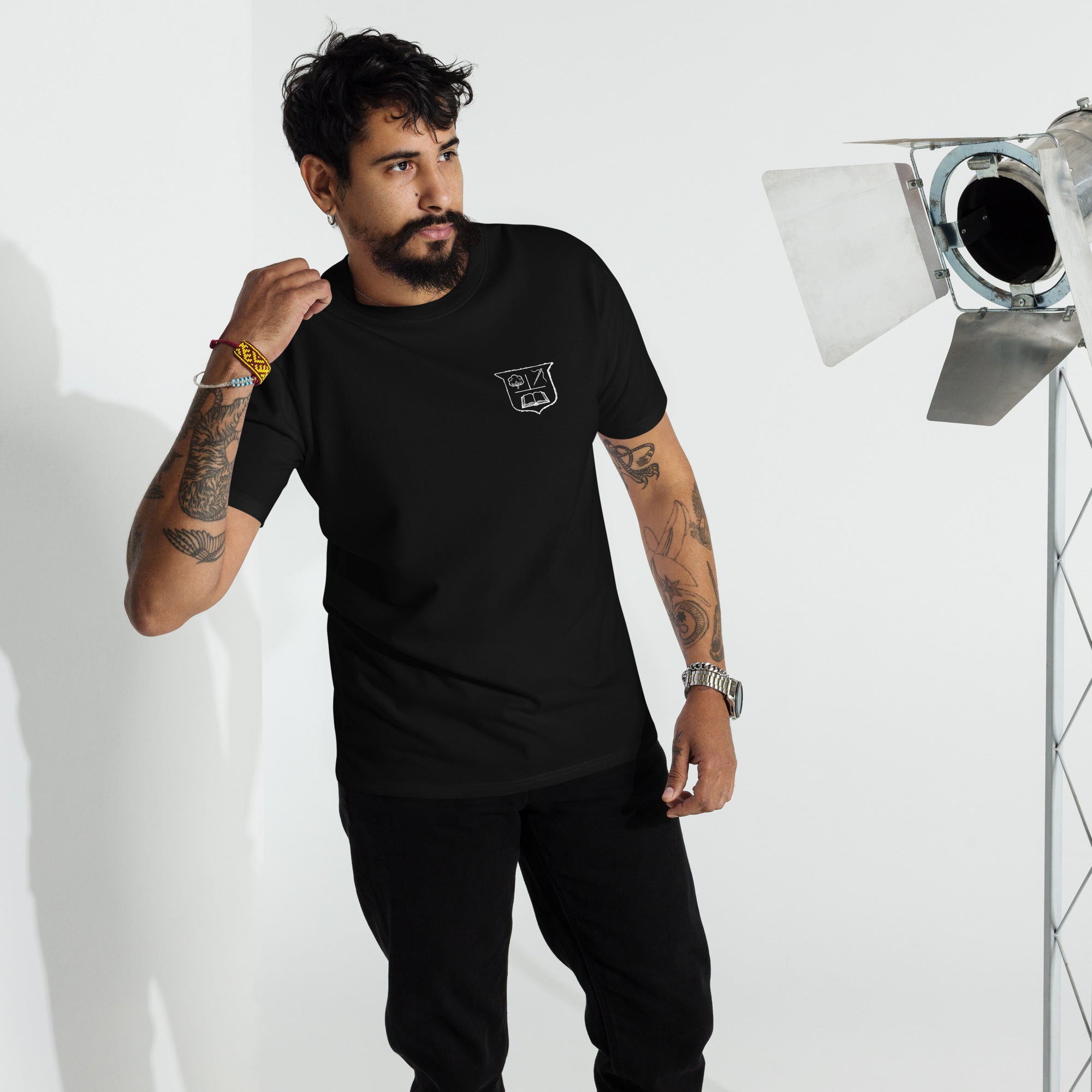 Man wearing a black t-shirt with a white crest on the left breast in a studio setting
