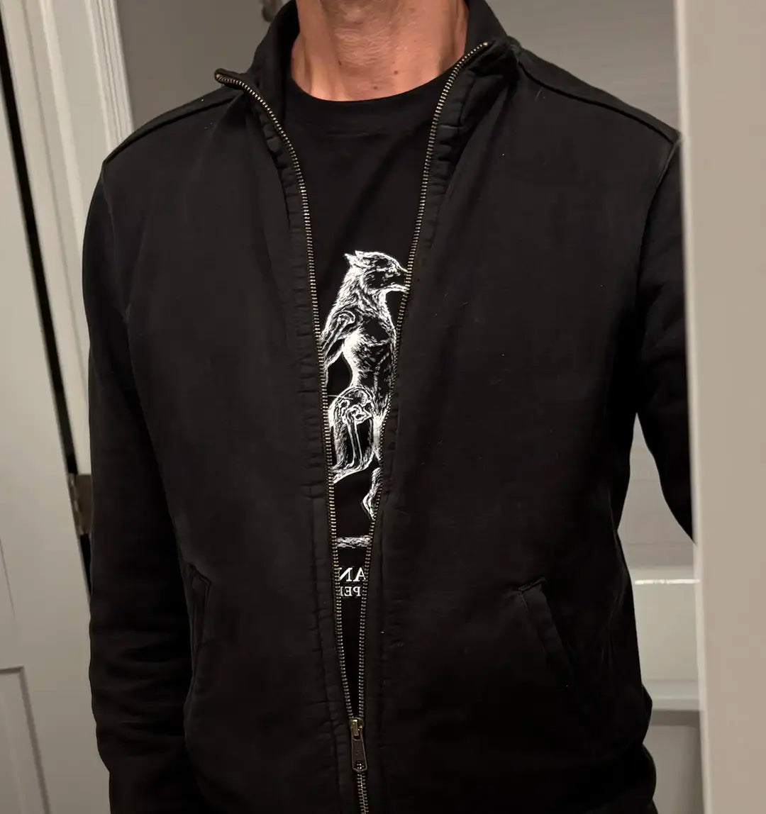 A person wearing a black zip-up hoodie over a black heavyweight all cotton graphic t-shirt with a white line art print of a hybrid man-dog anatomical drawing